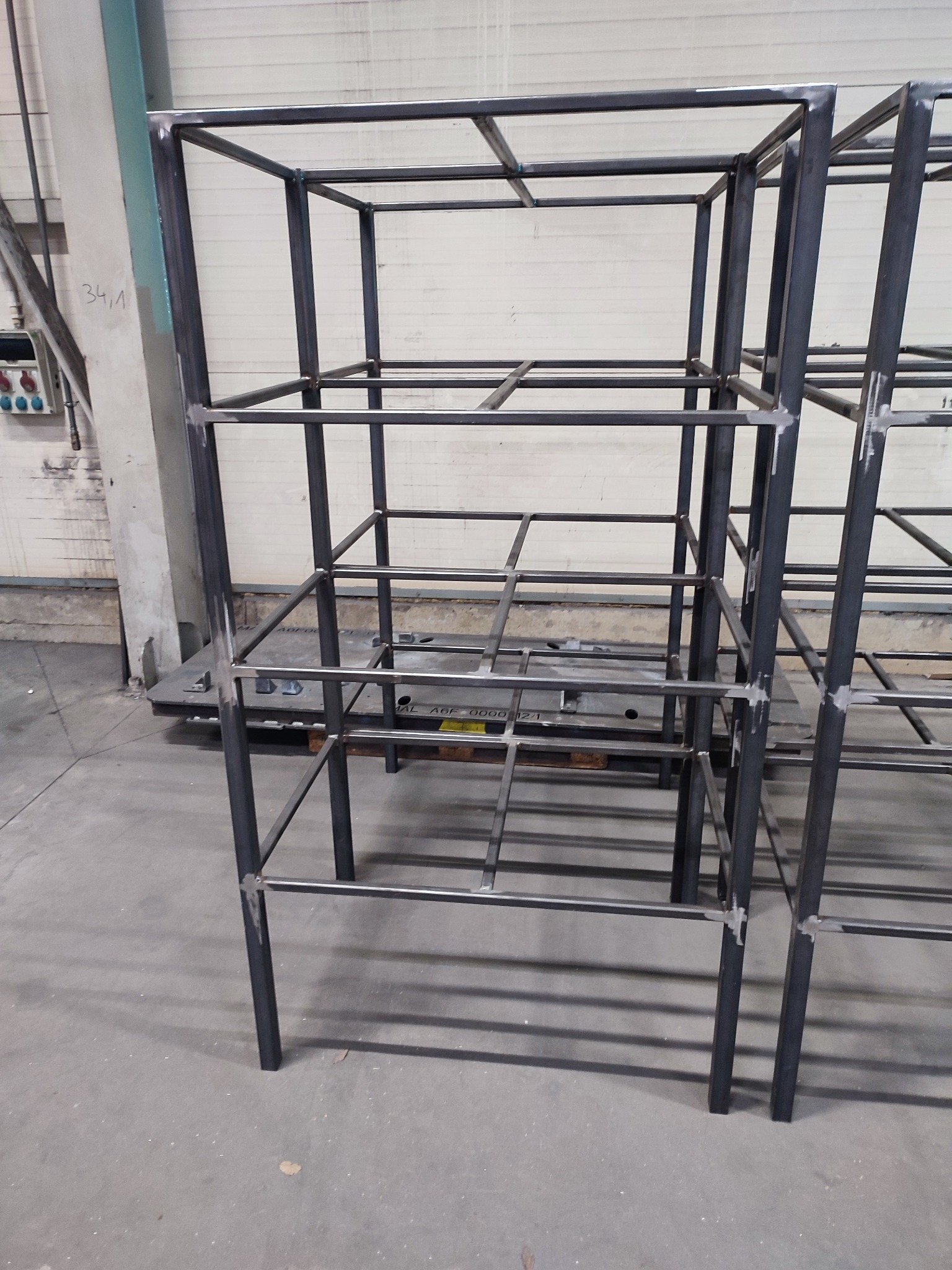 Surowa, metalowa konstrukcja szkieletowa z profili spawanych, prawdopodobnie element hali lub magazynu, widoczne ślady spawania, szary beton na podłodze.