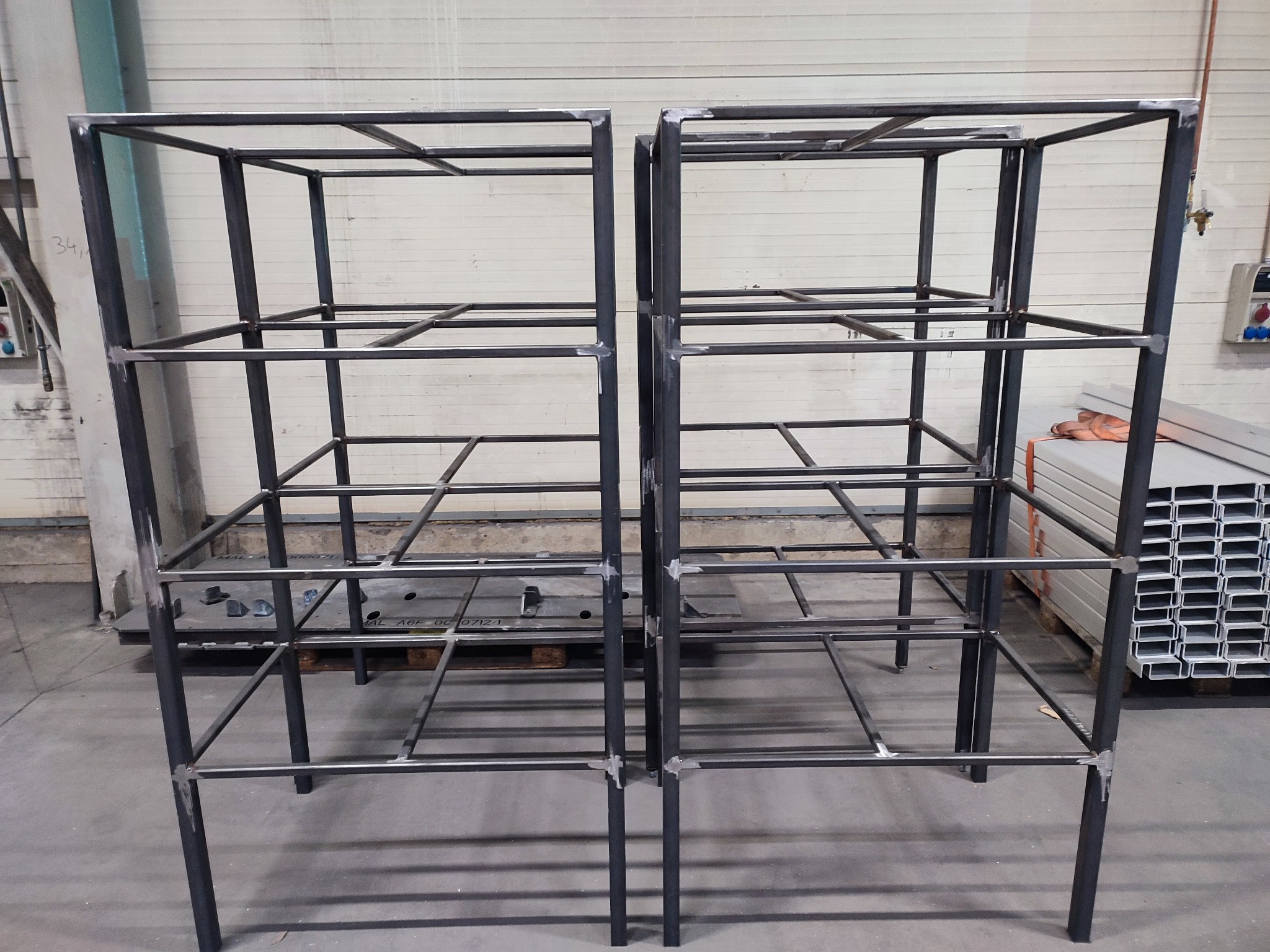 Dwie surowe, metalowe konstrukcje szkieletowe z profili, spawane, bez obróbki wykończeniowej, w hali produkcyjnej, z widocznymi śladami spawania.