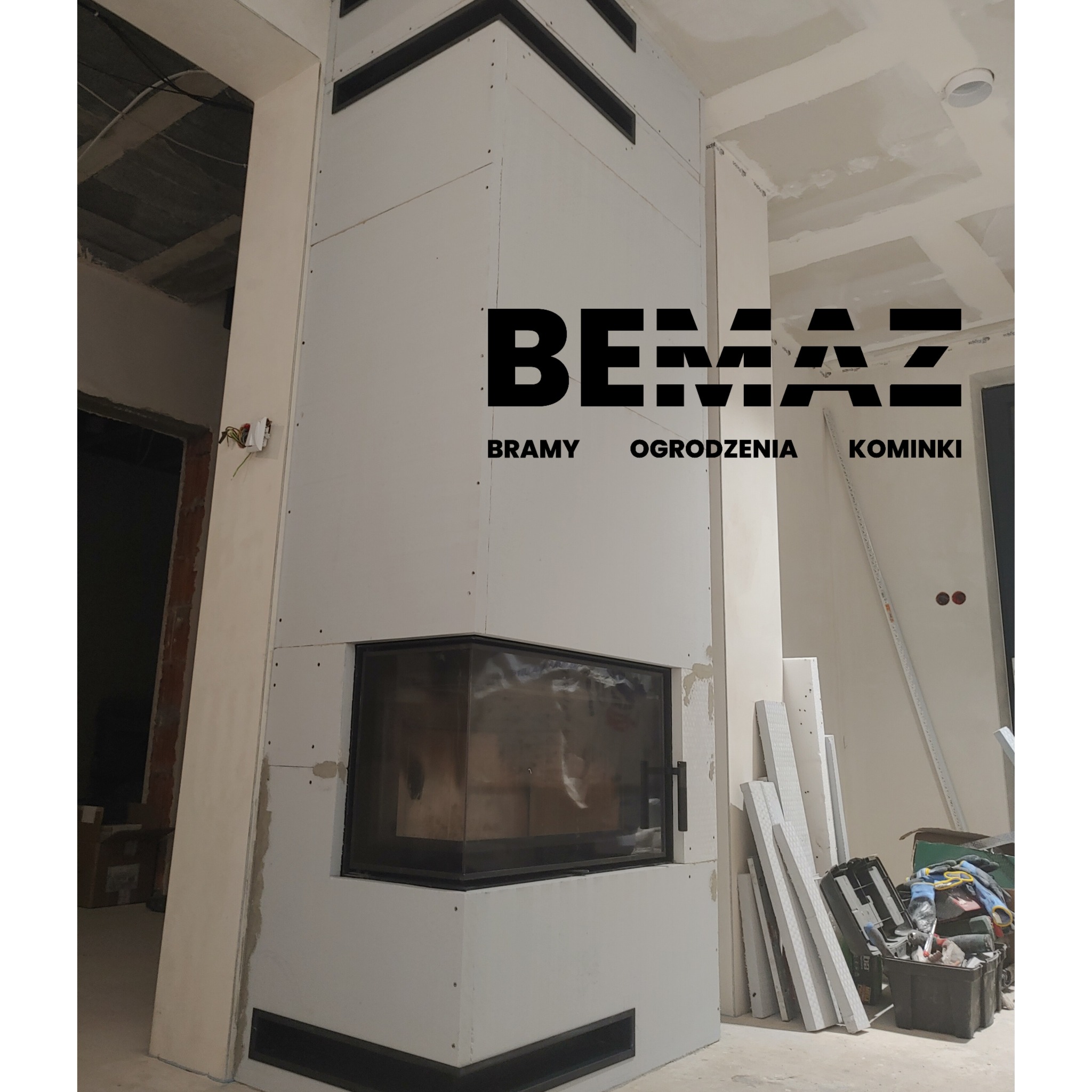 Niedokończona zabudowa kominka z wkładem, widoczne płyty gipsowo-kartonowe, czarna ramka wkładu i logo firmy na górze