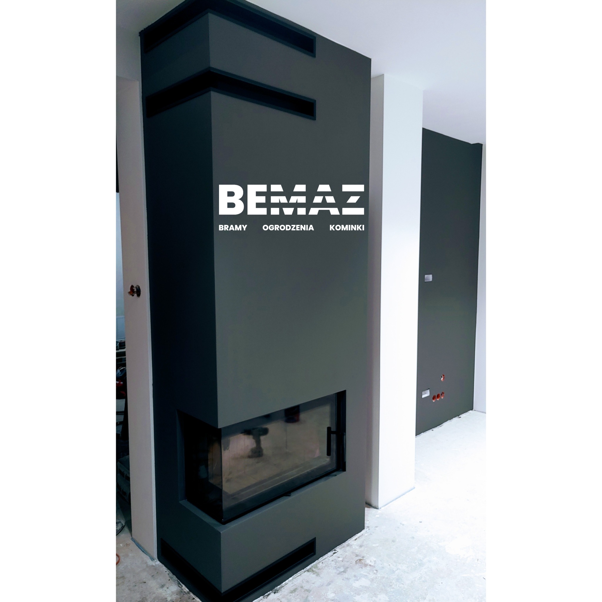 Nowoczesny, grafitowy kominek narożny z szybą, z logo firmy BEMAZ, prezentujący bramy, ogrodzenia i kominki, w surowym wnętrzu w trakcie wykończenia.