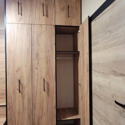 PU Sawa - Drewniana szafa wnękowa z czarnymi detalami i otwartymi drzwiami, ukazująca półki i drążek na ubrania. Widoczna struktura drewna na frontach.