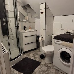 PU Sawa - Nowoczesna łazienka na poddaszu w Legnicy z kabiną prysznicową typu walk-in, umywalką z szafką i pralką. Biało-czarna kolorystyka, heksagonalna podłoga.