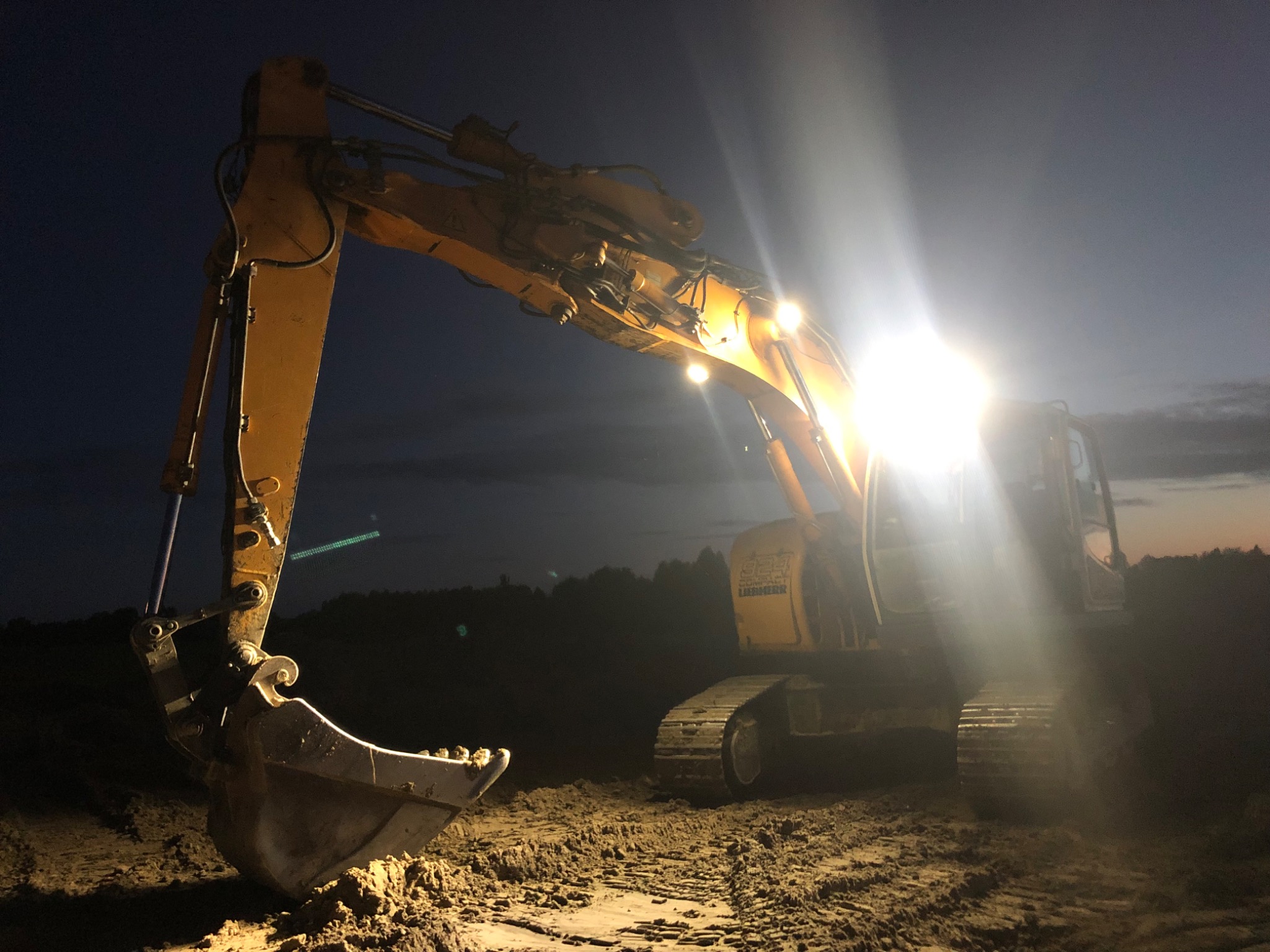 Żółta koparka Liebherr oświetlona reflektorami pracuje nocą na placu budowy, w tle ciemne niebo.