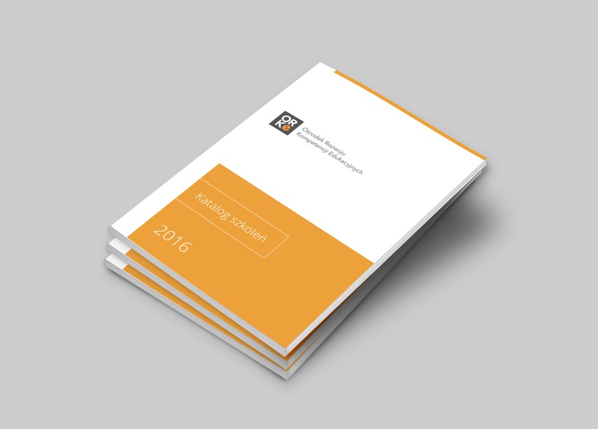 Stos katalogów szkoleń z pomarańczowym paskiem i rokiem 2016 na okładce, ułożonych na szarym tle.