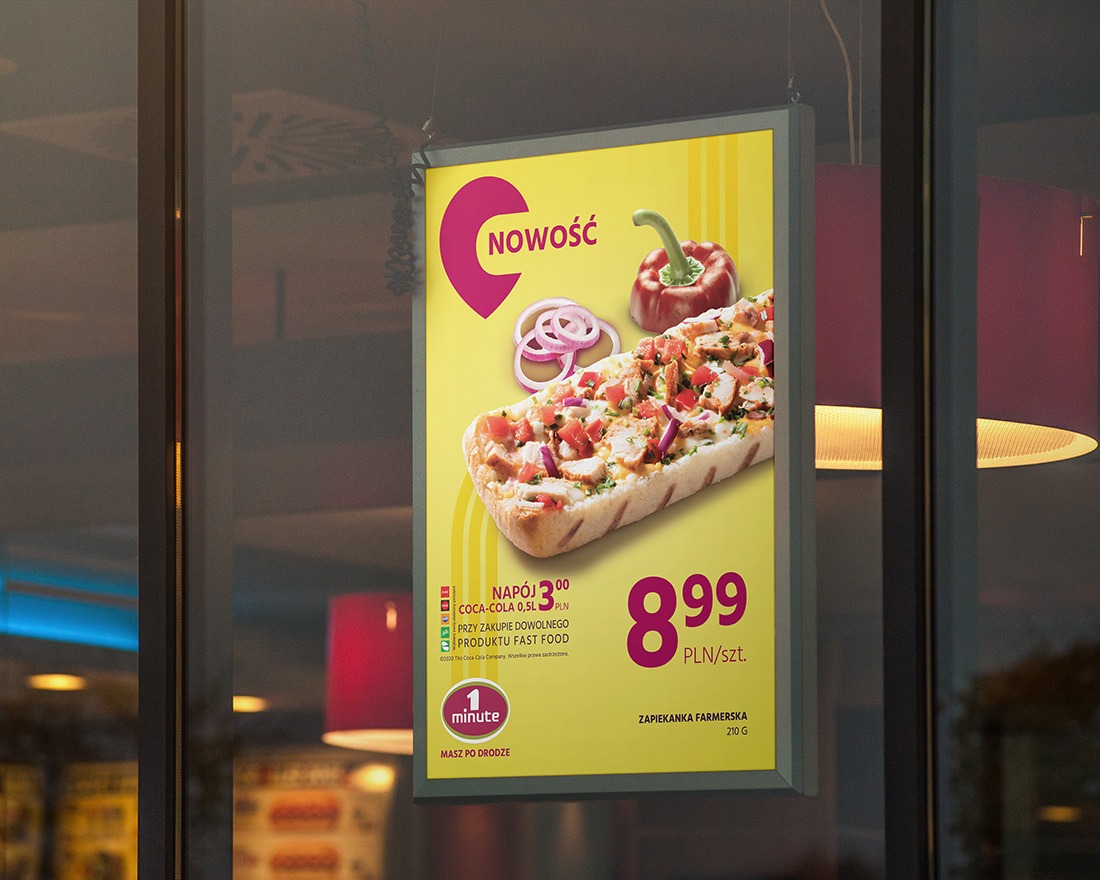 Plakat reklamowy zapiekanki farmerskiej z warzywami i napisem 'Nowość', wiszący na szklanej witrynie lokalu gastronomicznego, widoczne odbicia wnętrza.