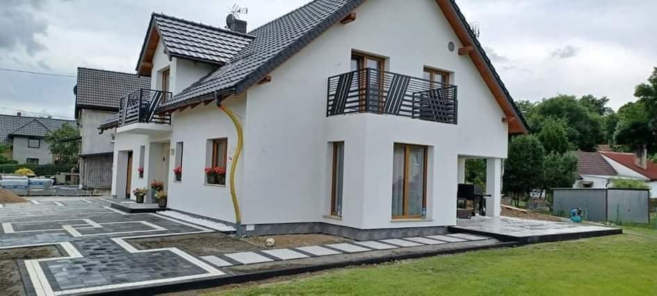 Nowoczesny dom jednorodzinny z wyłożonym geometrycznym wzorem z kostki brukowej i granitowej na podjeździe i tarasie.