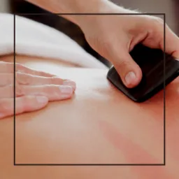 Gładki, czarny kamień w dłoni terapeuty przesuwany po plecach pacjenta, widoczne zaczerwienienia na skórze.