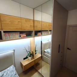 DESTO MEBLE - Nowoczesna szafa wnękowa z lustrzanymi drzwiami przesuwnymi i półkami na książki, oświetlenie LED podkreślające drewniane i białe fronty, szafka nocna z kwiatem, odbicie łóżka z szarym zagłówkiem.