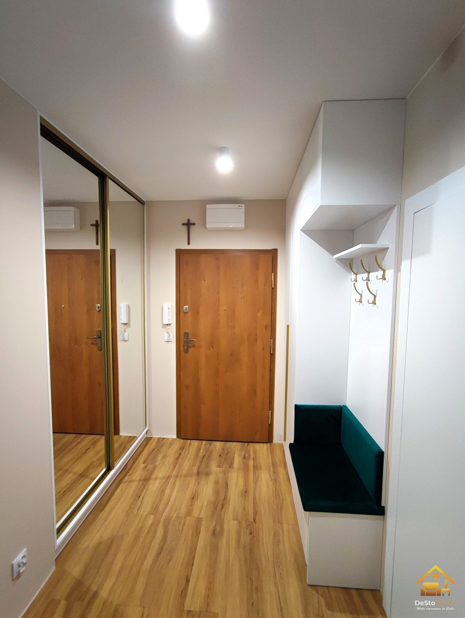 Aranżacja przedpokoju z lustrzaną szafą przesuwną, drewnianymi panelami podłogowymi, siedziskiem z zieloną tapicerką i wieszakami na ścianie.