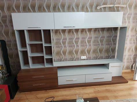 Nowoczesna meblościanka z białymi szafkami górnymi i brązowymi szufladami dolnymi, na tle ściany w wzorzyste tapety.