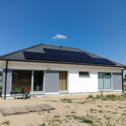 Ekobudowlanka - Nowoczesny dom jednorodzinny z szarym dachem i panelami słonecznymi na dachu, widok z zewnątrz, w oknie stoi pies rasy owczarek szwajcarski.