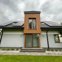 Nowoczesny dom jednorodzinny z panelami słonecznymi na dachu, widok z przodu, pochmurne niebo.