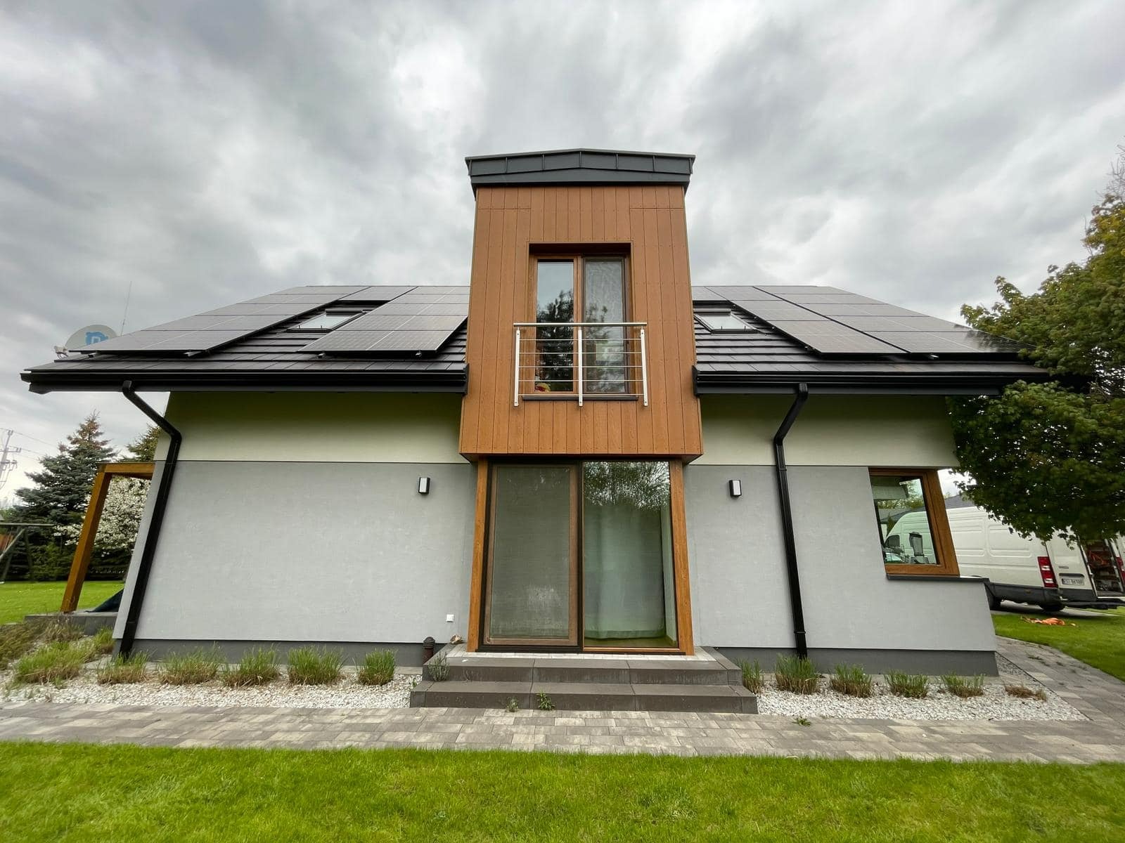 Nowoczesny dom jednorodzinny z panelami słonecznymi na dachu, widok z przodu, pochmurne niebo.
