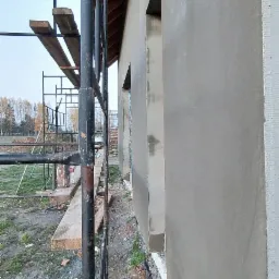 Świeżo otynkowana ściana budynku w Białymstoku, widoczne okna w stanie surowym i rusztowanie, przygotowane do dalszych prac wykończeniowych.