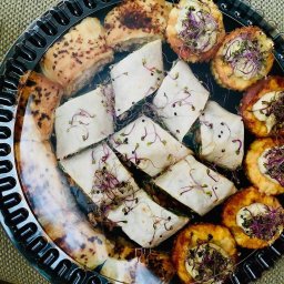 Kascatering - Elegancka taca z różnorodnymi przekąskami: roladki z kiełkami, tartaletki z kremem i ziołami, oraz pieczywo. Całość w czarnej, przezroczystej tacy.