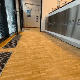 Parkiet ułożony w jodełkę, widoczne kratki wentylacyjne przy oknach, w tle recepcja z wygrawerowanymi współrzędnymi geograficznymi.