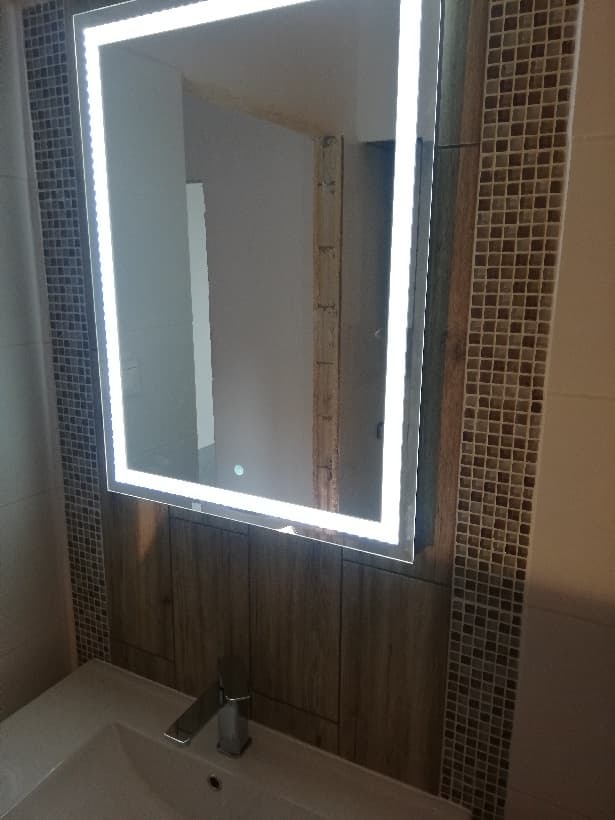 Wykończona łazienka w Poznaniu: nowoczesne lustro LED w ramie, umywalka z baterią, mozaika i drewnopodobne panele na ścianie.