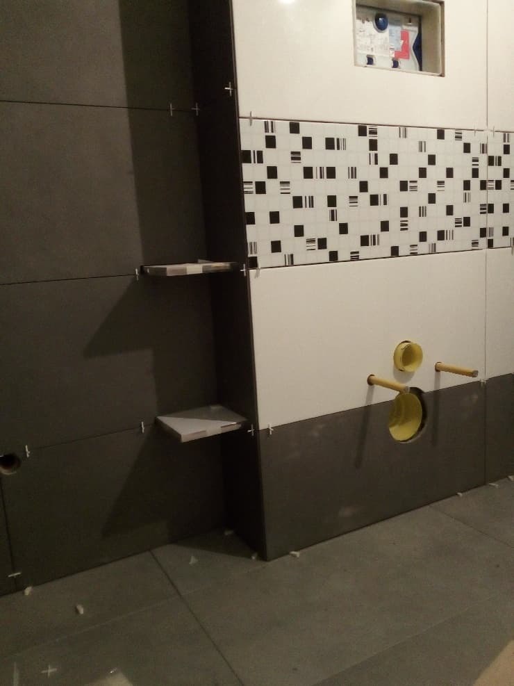 Świeżo wykafelkowana ściana łazienki z półkami w zabudowie, widoczne otwory na instalację sanitarną oraz wzorzysty pas płytek dekoracyjnych.