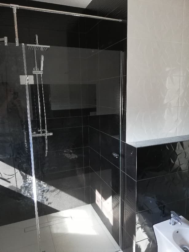 Nowoczesna kabina prysznicowa z czarnymi i białymi płytkami o zróżnicowanej fakturze, widoczny odpływ liniowy i biały bidet.