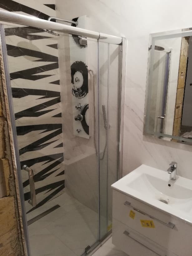 Nowoczesna kabina prysznicowa z czarno-białymi płytkami w geometryczne wzory, panel prysznicowy z hydromasażem i biała umywalka z szafką w wyremontowanej łazience.