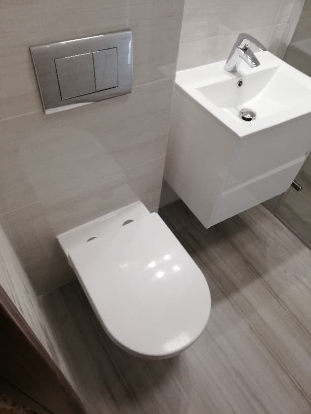 Nowoczesna łazienka: biała wisząca toaleta z deską wolnoopadającą, umywalka nablatowa z szafką w kolorze białym i chromowaną baterią, szara płytka imitująca drewno na podłodze i ścianach, srebrny...