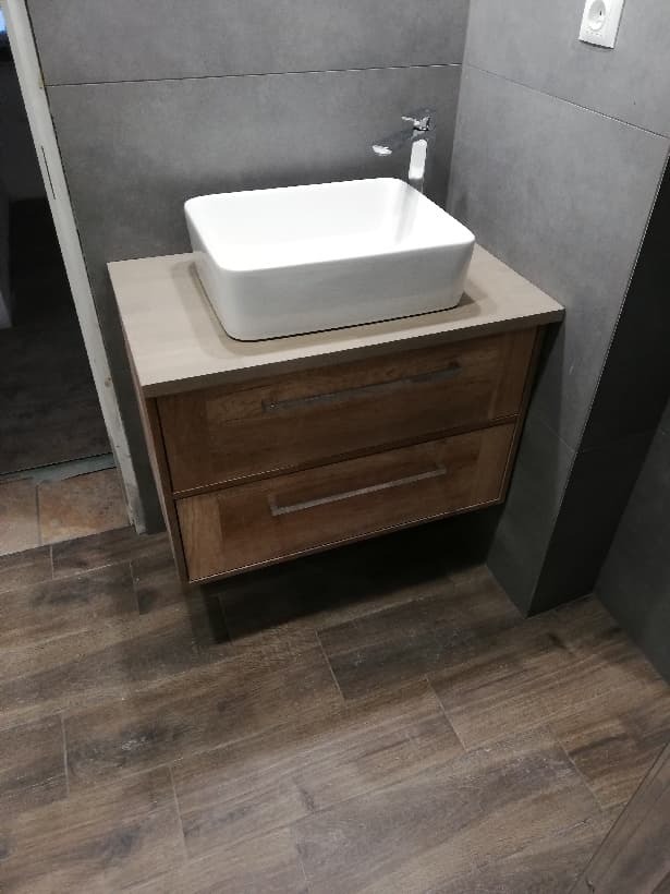 Nowoczesna łazienka z prostokątną umywalką nablatową, drewnianą szafką z szufladami i szarą płytką na ścianie.