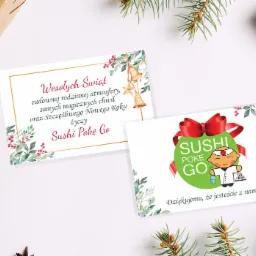 Dwie świąteczne kartki z życzeniami dla Sushi Poke Go, otoczone gałązkami świerku i prezentami na białym tle.
