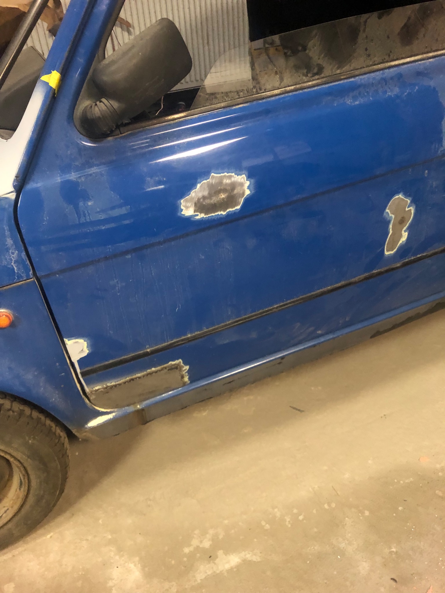 Niebieskie drzwi samochodu z widocznymi śladami korozji i szpachli, przygotowane do lakierowania.