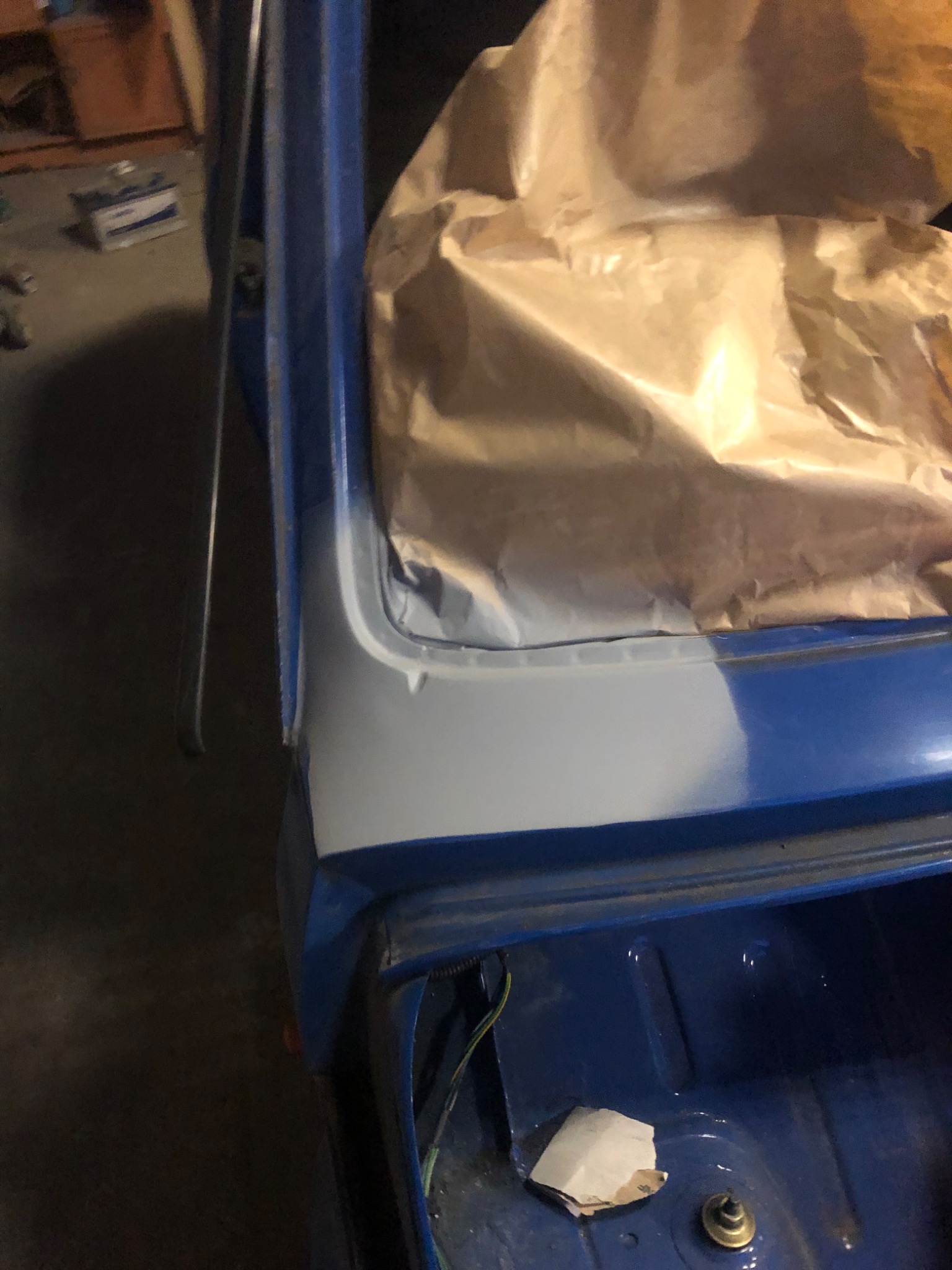 Fragment karoserii samochodu w trakcie naprawy blacharskiej, z widocznym świeżo nałożonym szpachlem i papierem maskującym, przygotowany do dalszych prac lakierniczych.