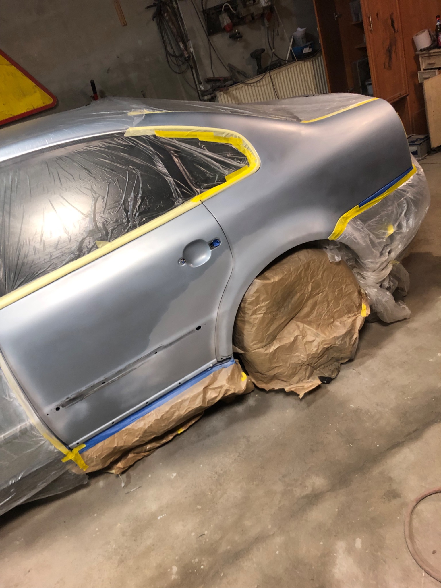 Przygotowany do lakierowania samochód zabezpieczony folią, papierem i taśmą malarską w warsztacie.