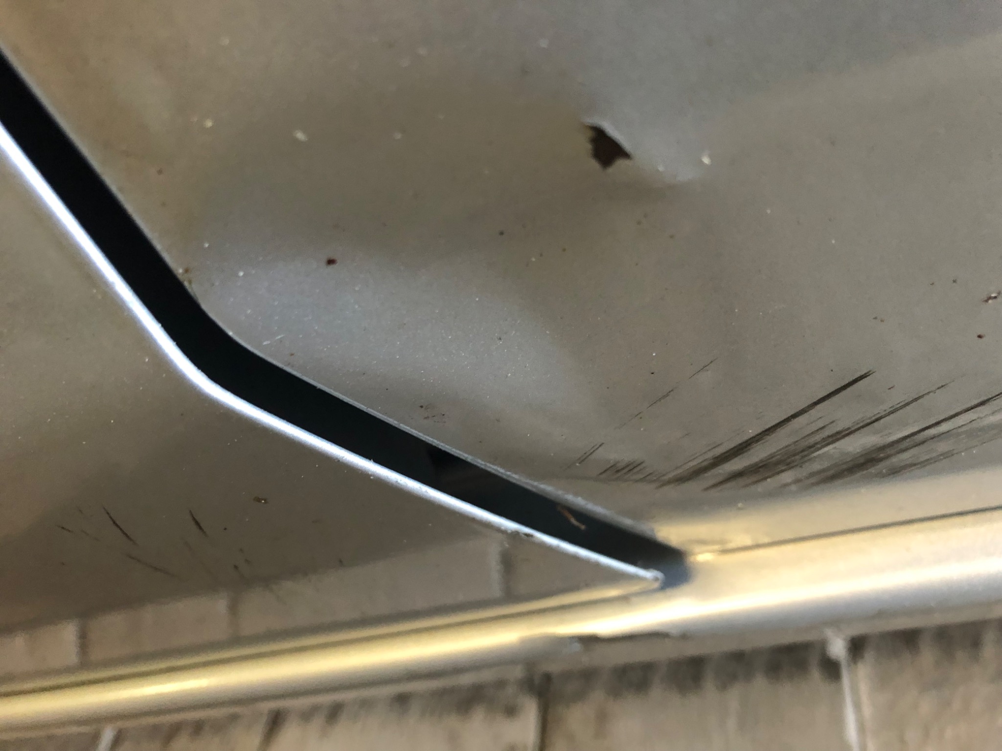 Zbliżenie na fragment skorodowanej karoserii samochodu w Strzepczu, widoczne rysy i ogniska rdzy na powierzchni lakieru oraz w szczelinie między elementami nadwozia.