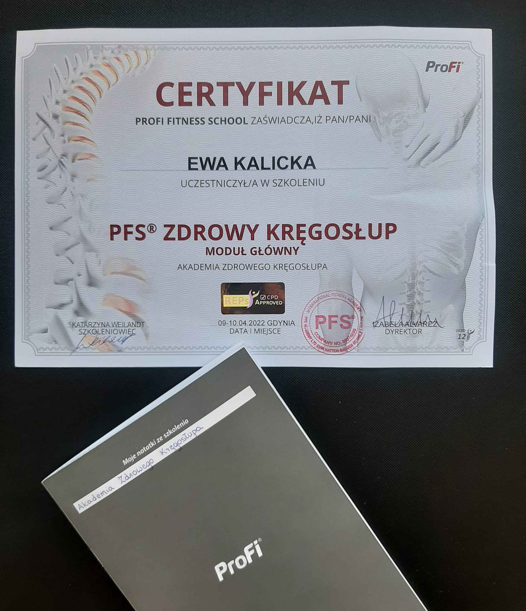 Certyfikat ukończenia szkolenia 'Zdrowy Kręgosłup' Akademii Zdrowego Kręgosłupa, wydany przez Profi Fitness School dla Ewy Kalickiej, leżący obok notatnika z dopiskiem 'Moje notatki ze szkolenia...