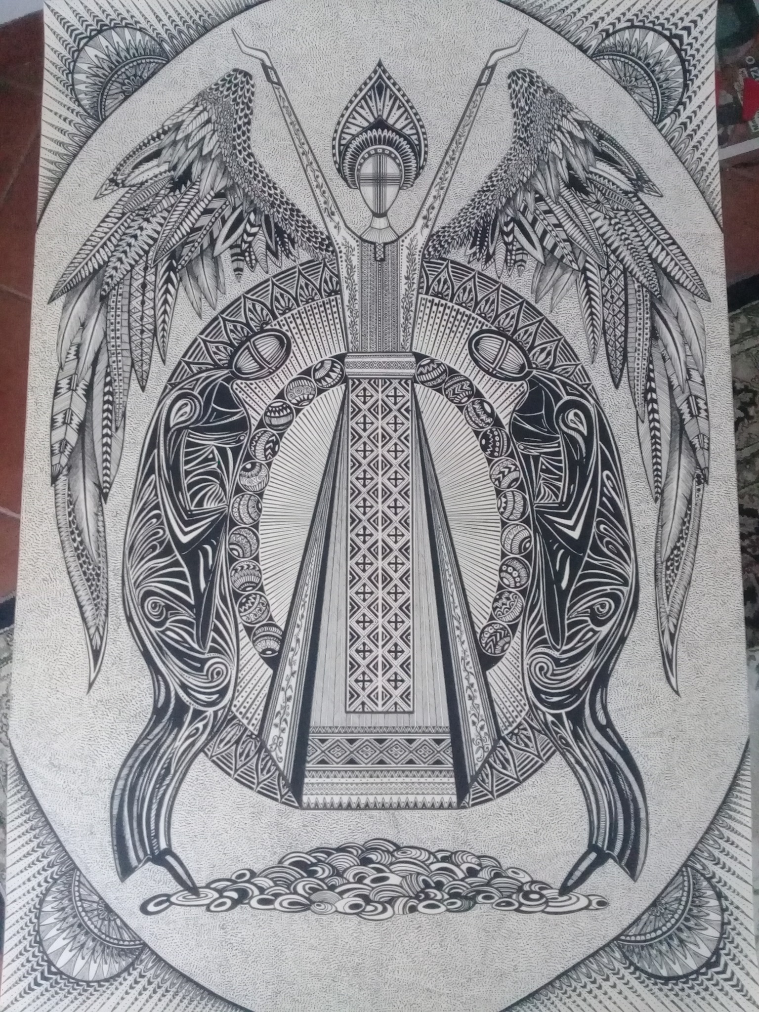 Czarno-biały rysunek przedstawiający stylizowaną postać anioła z rozłożonymi skrzydłami, otoczonego ornamentami i wzorami geometrycznymi, wykonany drobnymi kreskami na szarym tle.