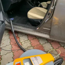 Wnętrze samochodu z jasną tapicerką poddawane czyszczeniu za pomocą profesjonalnego odkurzacza ekstrakcyjnego marki Ghibli & Wirbel Power Extra, widoczna dysza w dywaniku i wąż urządzenia na tle...