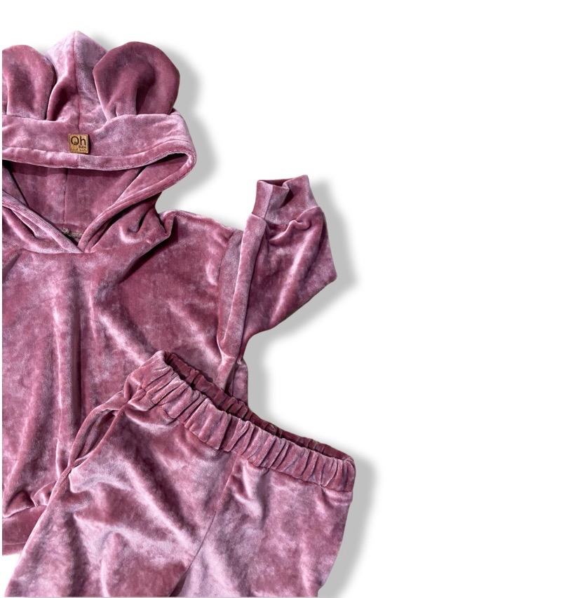 Dziecięcy welurowy komplet dresowy w odcieniu pudrowego różu, bluza z kapturem z uszami misia, na kapturze mała metka z logo, spodnie z elastyczną gumką w pasie, na białym tle.