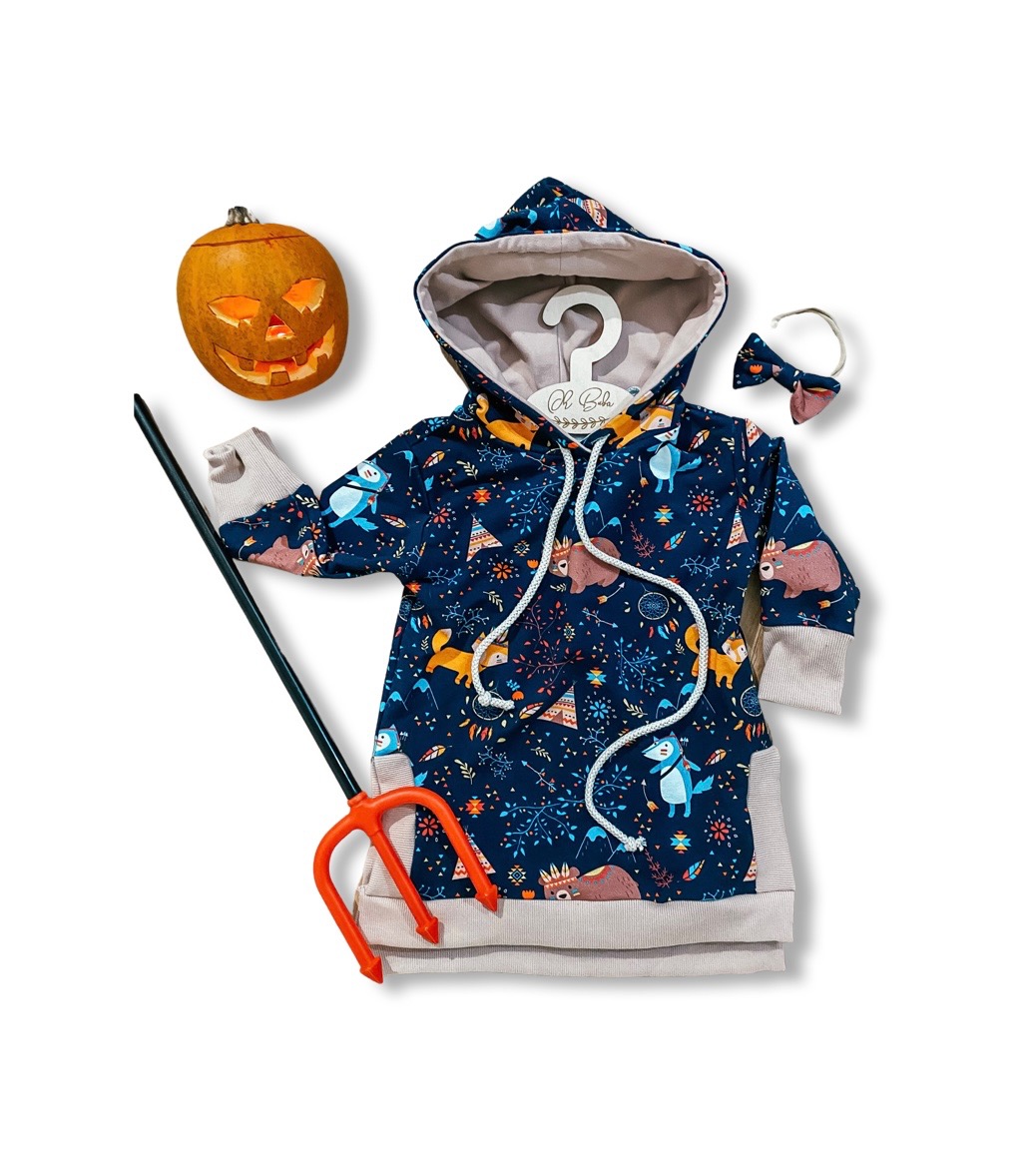 Dziecięca sukienka z kapturem w leśne zwierzęta, zawieszona na wieszaku, z dynią Halloween, trójzębem i opaską z kokardką na białym tle.