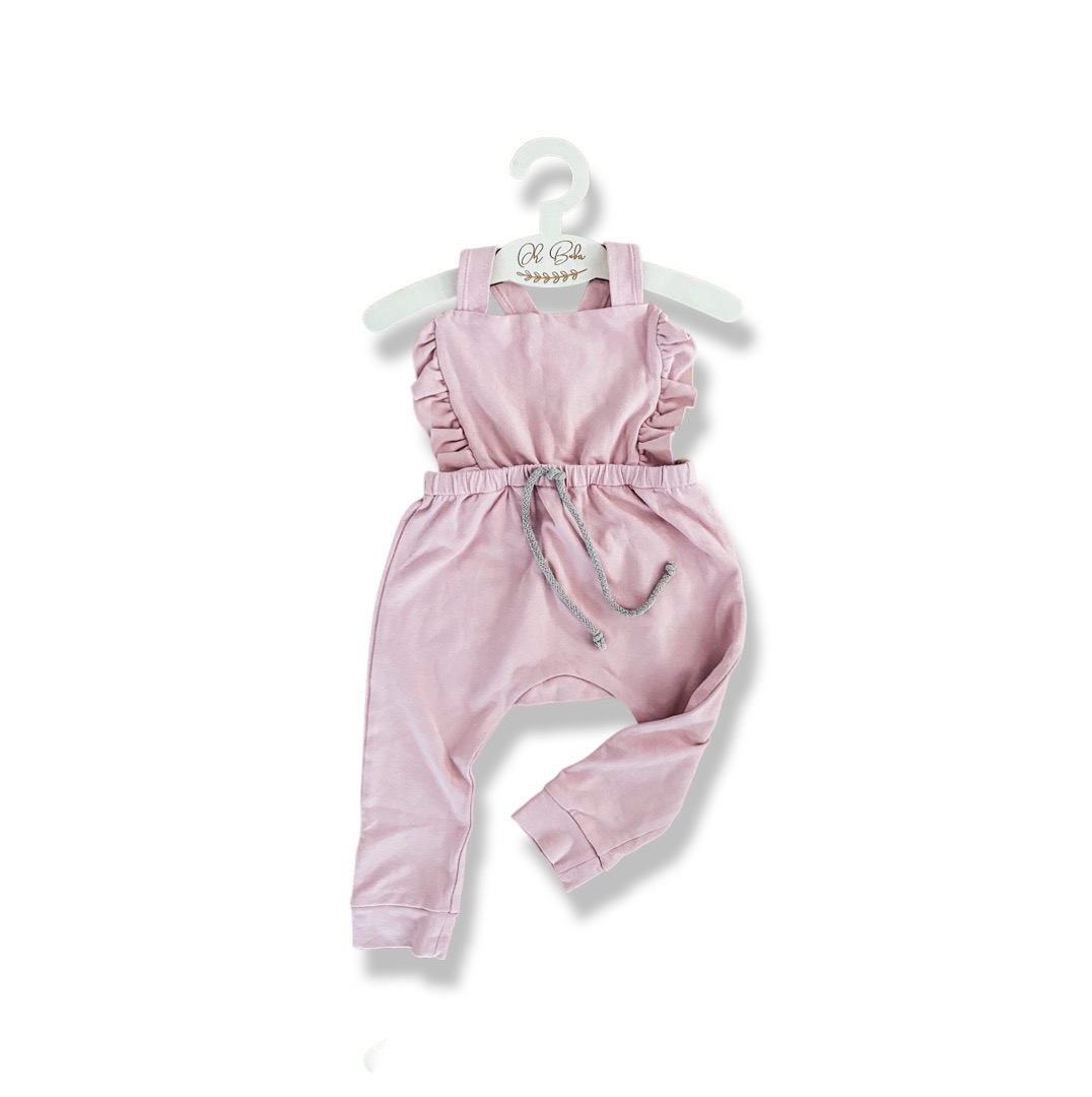 Różowy bawełniany rampers dziecięcy z falbankami i sznurkiem w pasie, wiszący na białym wieszaku z napisem 'Oh Baby' na białym tle.