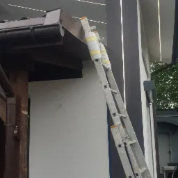 Świeżo pomalowana elewacja domu z brązowymi elementami, drabina oparta o ścianę, zabezpieczona pianką i taśmą, widoczne ślady po przewodach na ścianie.