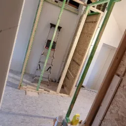 Montaż stelaża z płyt karton gips w skośnym pomieszczeniu poddasza, widoczne narzędzia i drabina.