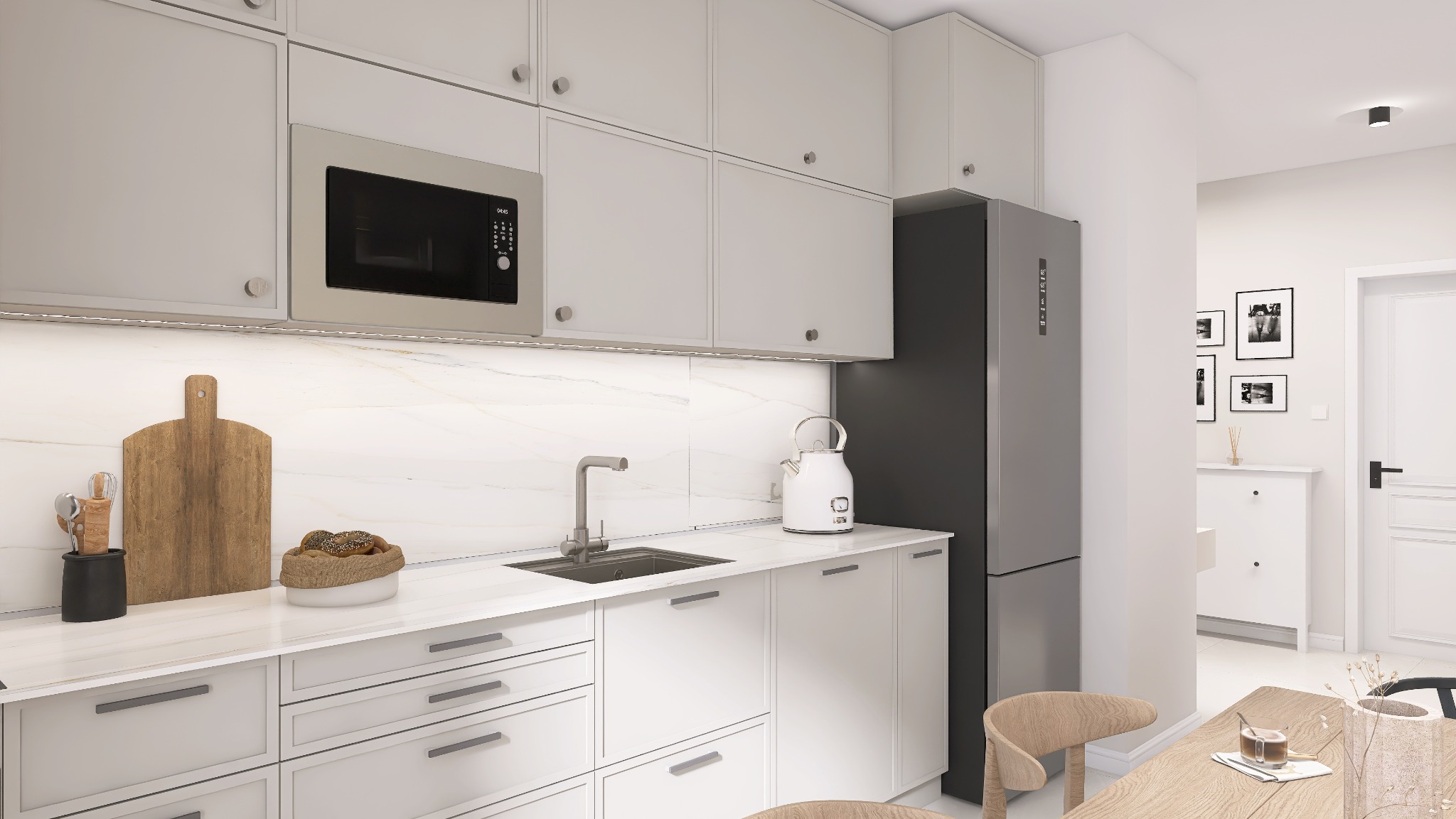 Nowoczesna kuchnia w odcieniach bieli i szarości z drewnianymi akcentami, wyposażona w zabudowane szafki, mikrofalówkę, zlew, czajnik elektryczny, deskę do krojenia i akcesoria kuchenne,...