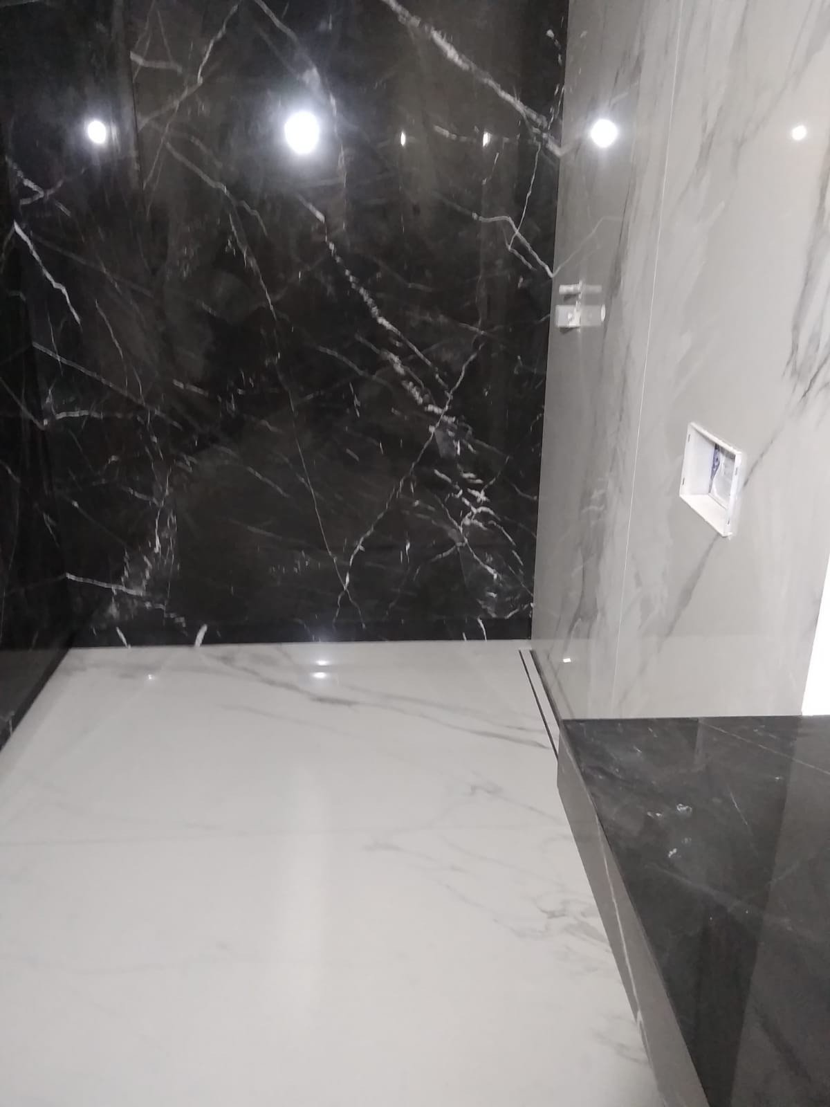 Nowoczesna łazienka z czarno-białymi marmurowymi płytkami na ścianach i podłodze, widoczne gniazdko elektryczne.