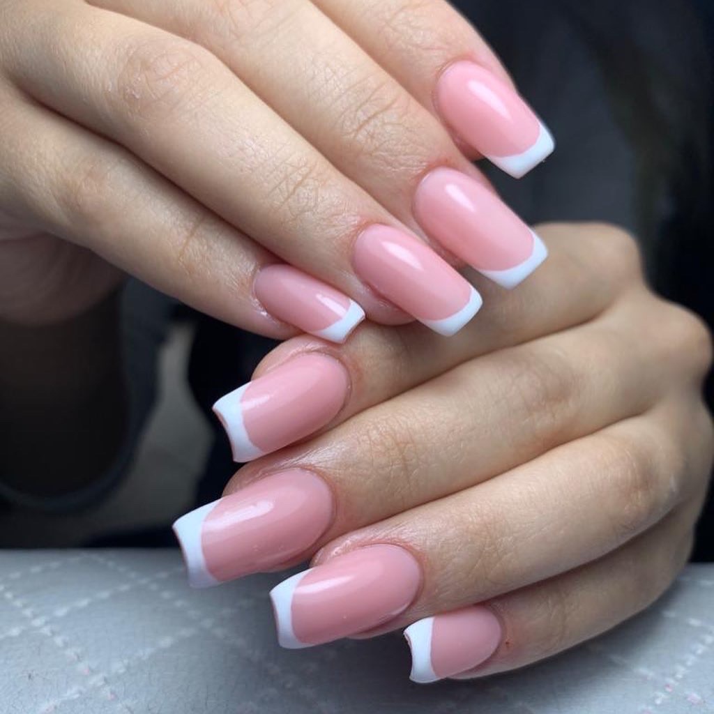 Delikatny różowy manicure hybrydowy z białym french na kwadratowych paznokciach, widoczne dłonie na jasnym tle.