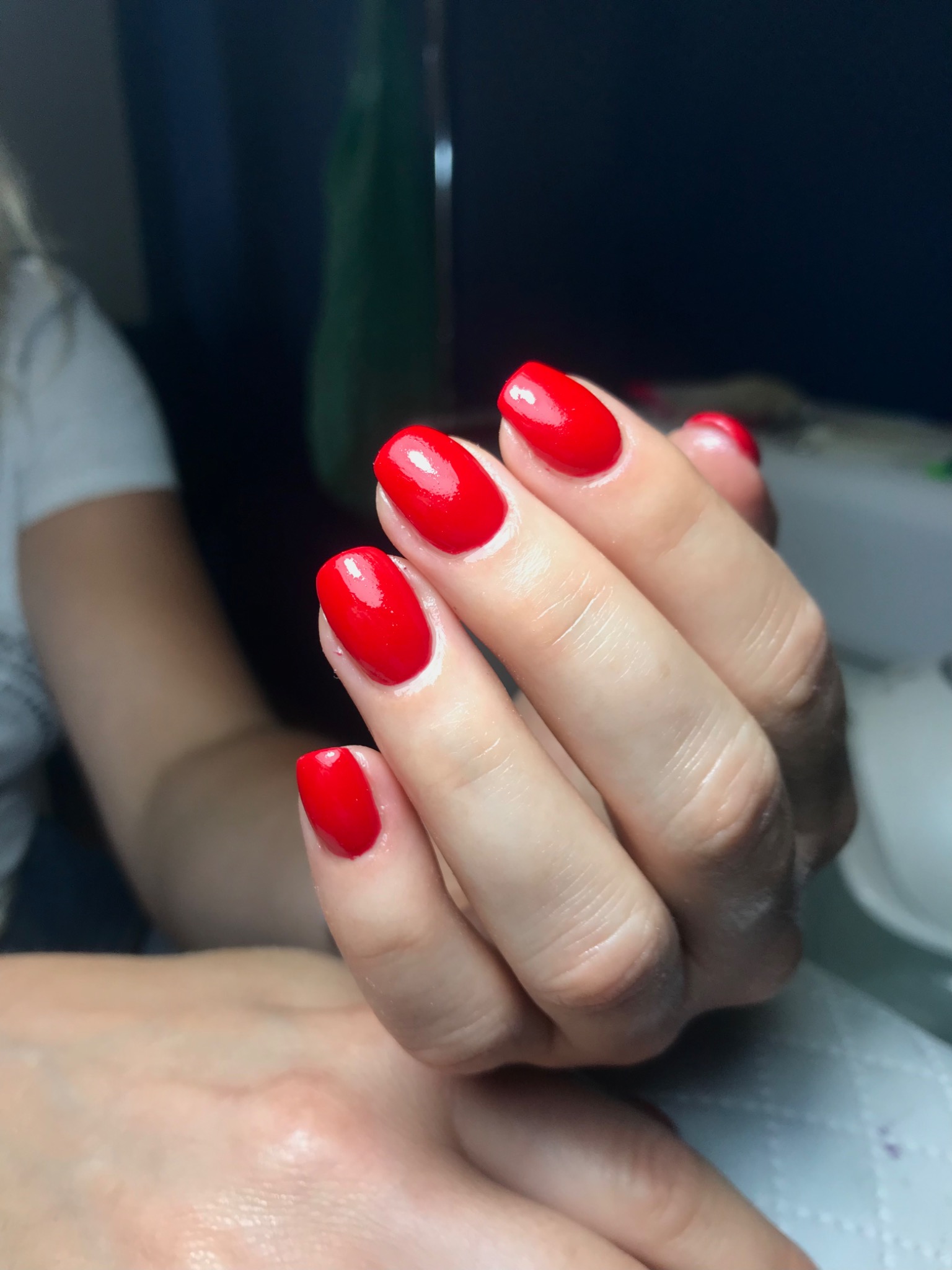 Dłoń z pomalowanymi na intensywny czerwony kolor, owalnymi paznokciami. Widoczne delikatne linie na skórze dłoni, a tło rozmyte.