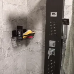 Nowoczesna kabina prysznicowa z czarnym panelem natryskowym, półką na kosmetyki i szarymi płytkami imitującymi marmur