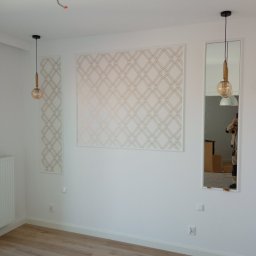 Serhii Pobokov - Wykończone wnętrze pokoju z panelami dekoracyjnymi w geometryczny wzór, wiszącymi lampami z okrągłymi kloszami i lustrem w białej ramie, ukazującym odbicie osoby robiącej zdjęcie.