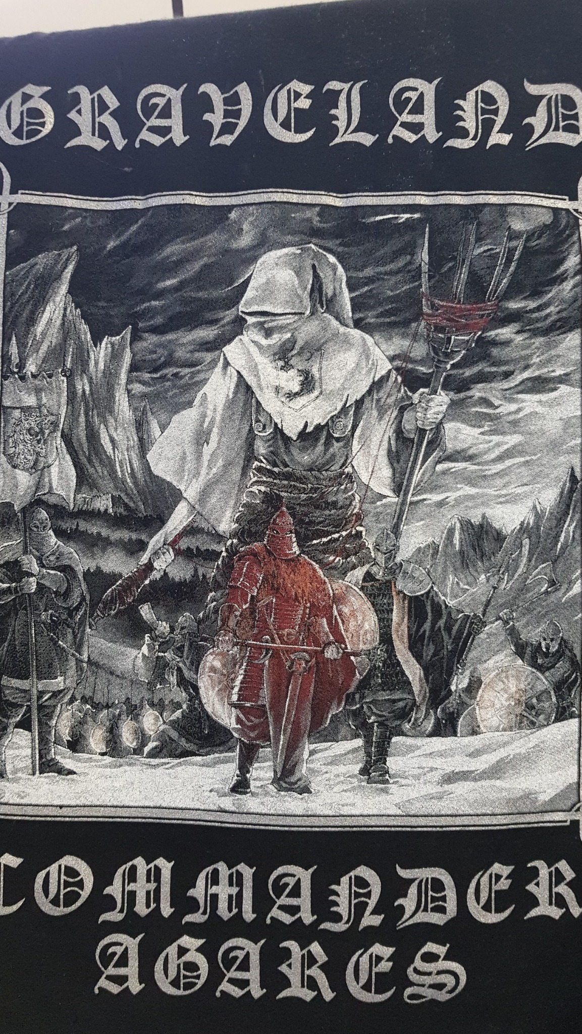 Czarna koszulka z nadrukiem fantasy przedstawiającym postacie w zbrojach i szatach na tle górskiego krajobrazu, z napisem GRAVELAND COMMANDER AGARES.