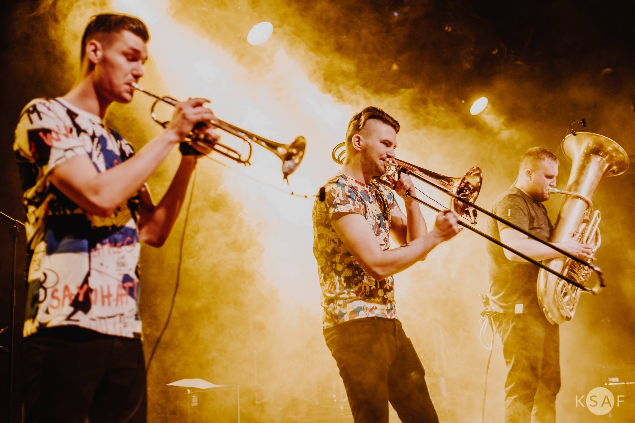 Zespół muzyczny grający na trąbce, puzonie i tubie podczas występu na scenie w oświetleniu scenicznym.
