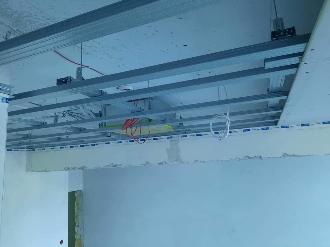 Metalowa konstrukcja sufitu podwieszanego z widocznymi kablami i przewodami elektrycznymi w trakcie montażu, widok z wnętrza remontowanego pomieszczenia w Sejnach.