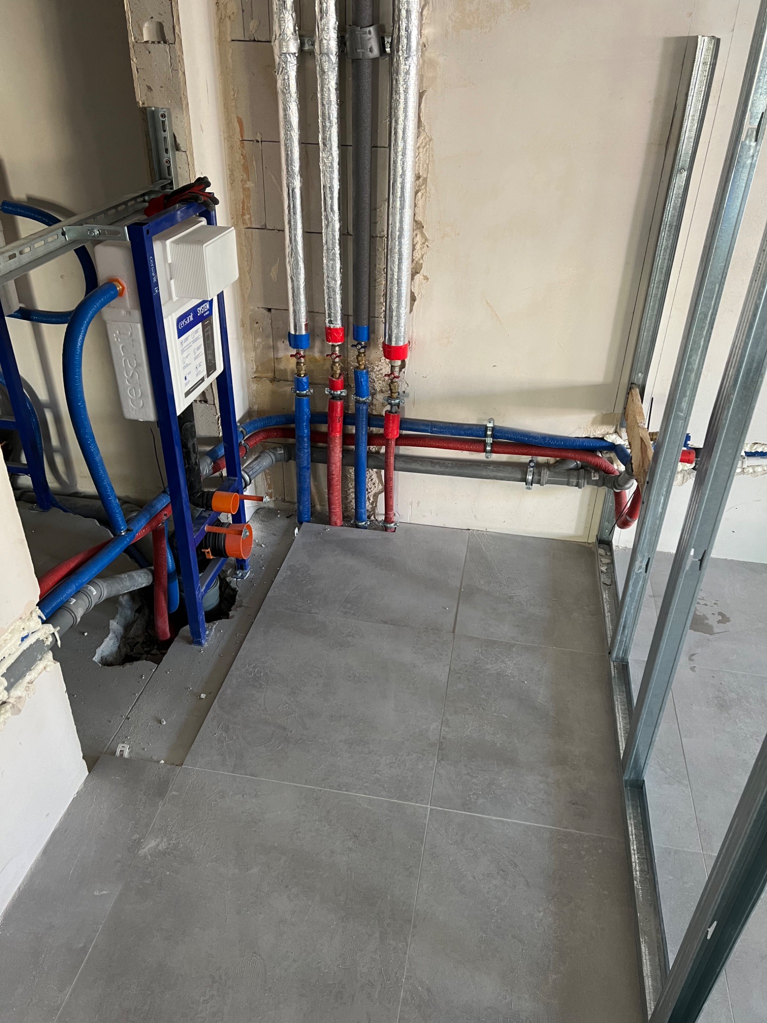 Instalacja podtynkowa WC Cersanit w trakcie montażu, widoczne rury doprowadzające wodę, odpływ kanalizacyjny i profile do zabudowy ściany działowej.