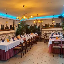 Uroczysta sala restauracyjna z nakrytymi stołami, białe obrusy z różowym akcentem, niebieskie oświetlenie LED na suficie, żyrandole w stylu retro, przygotowana na przyjęcie.